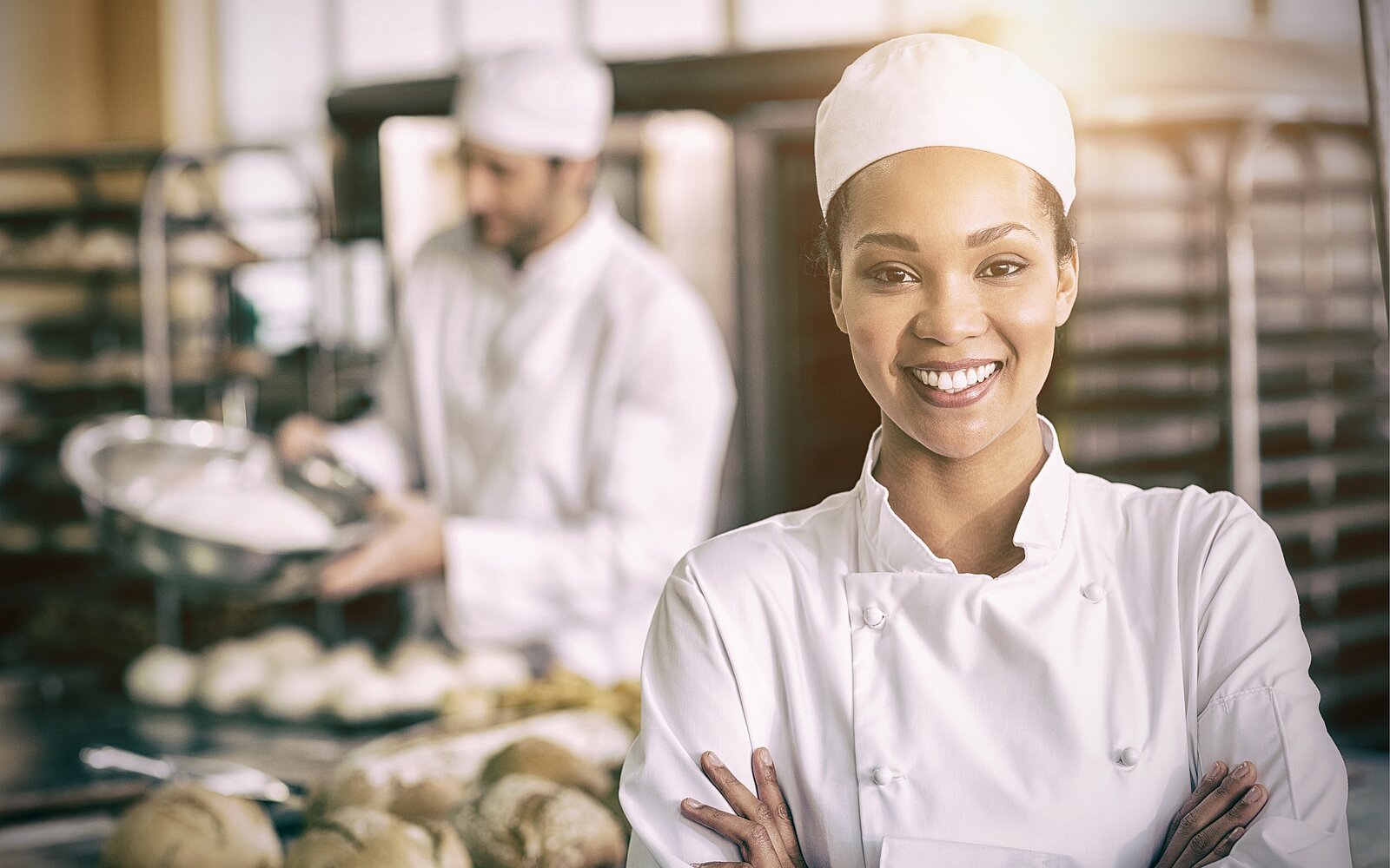 eine Bäckerin die lächelt, im Hintergrund ein Bäcker, der eine Schüssel in der Hand hält