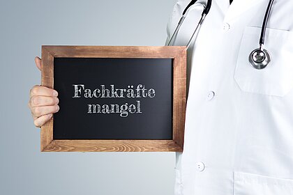 Mediziner, der eine Tafel mit dem Wort Fachkräftemangel in der Hand hält