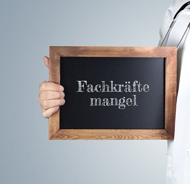Mediziner, der eine Tafel mit dem Wort Fachkräftemangel in der Hand hält