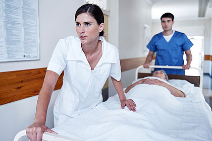 Krankenschwester und Pfleger schieben Patienten im Bett den Krankenhausflur entlang.
