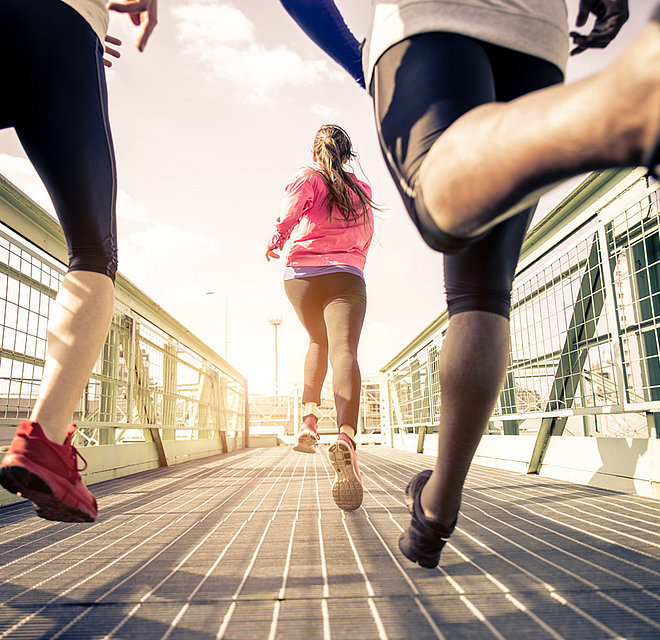 Das Bild zeigt Jogger von hinten, die über eine Brücke laufen.