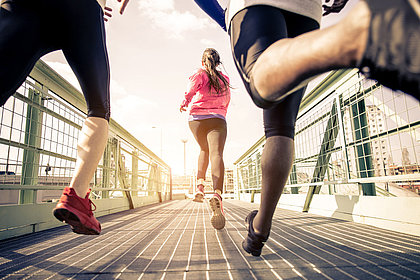 Das Bild zeigt Jogger von hinten, die über eine Brücke laufen.