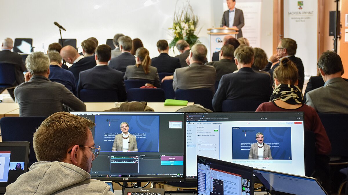 Monitore vor Publikum und einem Redner