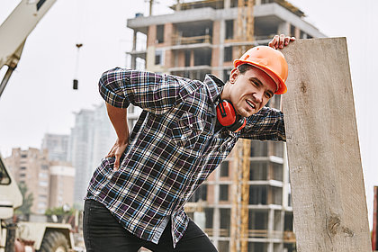  Bauarbeiter im Schutzhelm mit Rückenschmerzen bei der Arbeit auf der Baustelle.