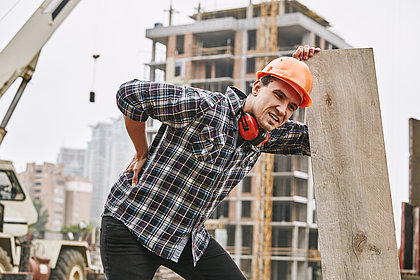  Bauarbeiter im Schutzhelm mit Rückenschmerzen bei der Arbeit auf der Baustelle.