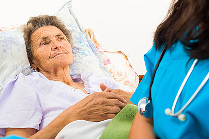 Eine Krankenschwester sitzt am Bett einer älteren Patientin.