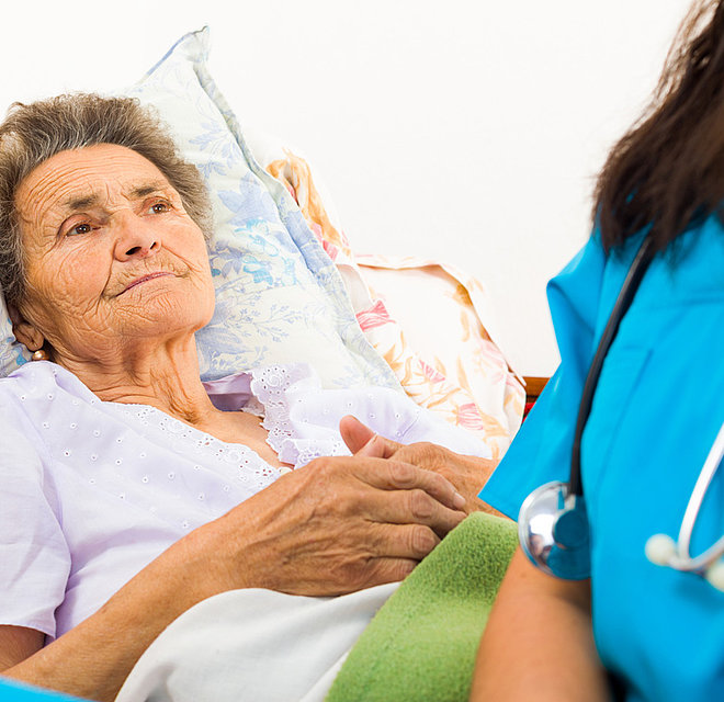 Eine Krankenschwester sitzt am Bett einer älteren Patientin.